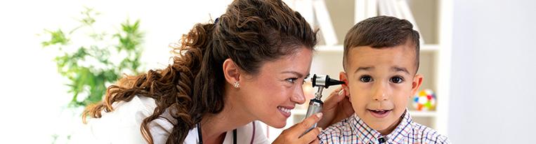 A health care provider looks into a young boy's ear with an otoscope.