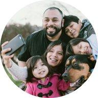 A family of 2 adults, 3 children, and a dog huddle together smiling for a selfie